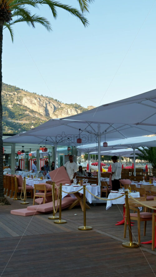 Video - Menton, France - September 4, 2024: Palm trees near a restaurant on the beach. Vertical