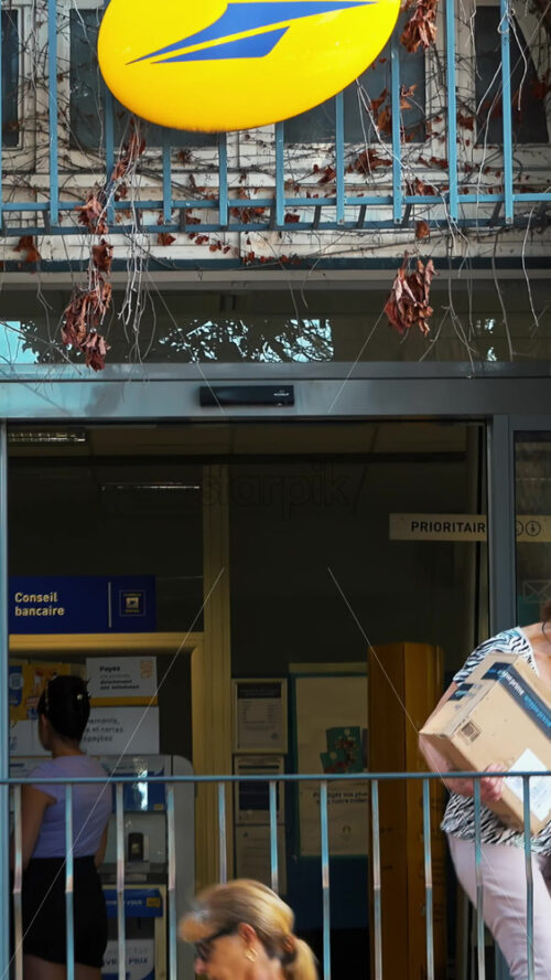 Video - Menton, France - September 4, 2024: Woman walking out a Post office with a package in daylight. Vertical
