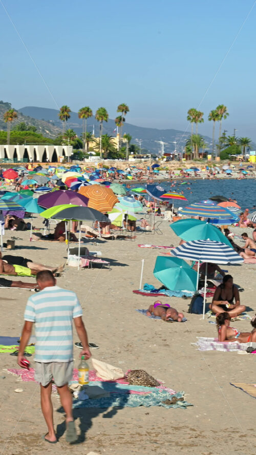 Video - Menton, France - September 4, 2024: People swimming and relaxing on the beach under sun umbrellas. Vertical