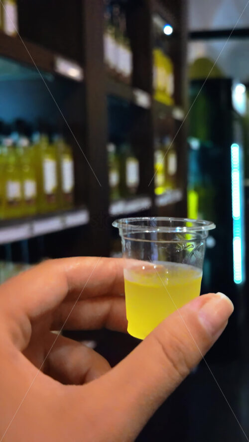 Video - Close up of a woman's hand holding a shot of limoncello in a store. Vertical
