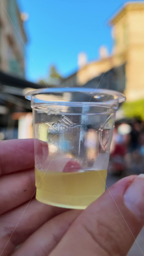 Video - Close up of a woman's hand holding a shot of limoncello on the streets of Menton, France. Vertical