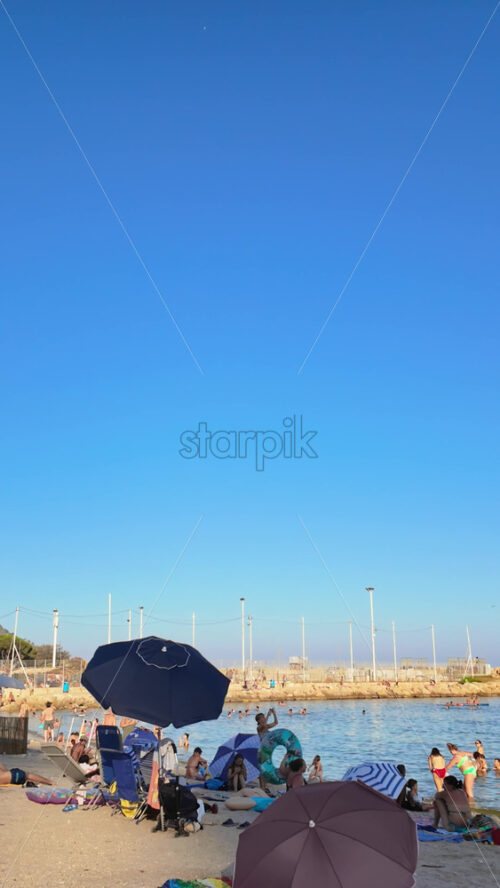 Video - Menton, France - September 4, 2024: People swimming and relaxing on the beach under sun umbrellas. Vertical