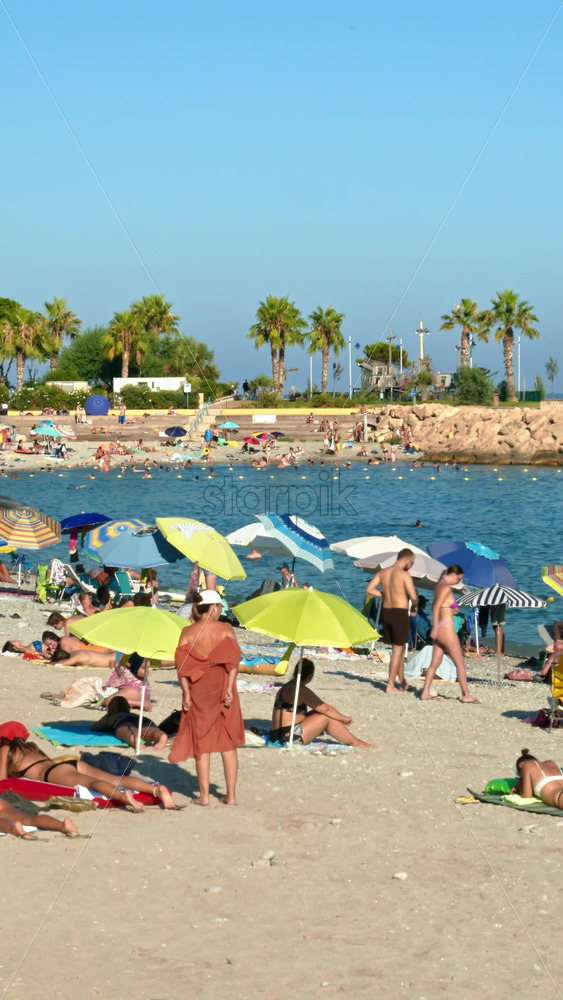 Video - Menton, France - September 4, 2024: People swimming and relaxing on the beach under sun umbrellas. Vertical