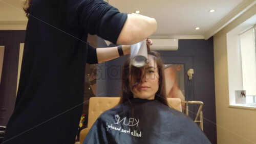Video - Chisinau, Moldova - April 15, 2021: Hairdresser wearing mask styling woman's hair at the salon