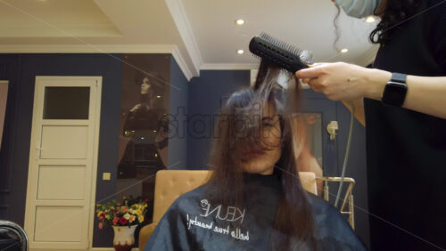 Video - Chisinau, Moldova - April 15, 2021: Hairdresser wearing mask styling woman's hair at the salon