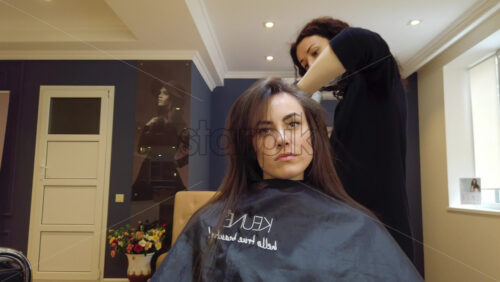 Video - Chisinau, Moldova - April 15, 2021: Hairdresser wearing mask styling woman's hair at the salon