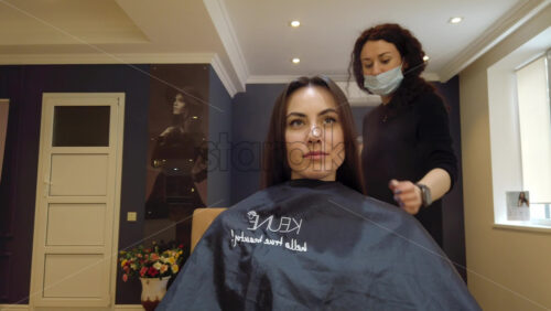 Video - Chisinau, Moldova - April 15, 2021: Hairdresser wearing mask styling woman's hair at the salon