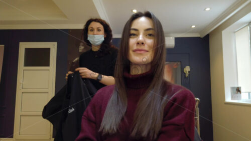Video - Chisinau, Moldova - April 15, 2021: Hairdresser wearing mask styling woman's hair at the salon
