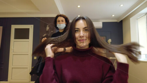 Video - Chisinau, Moldova - April 15, 2021: Hairdresser wearing mask styling woman's hair at the salon