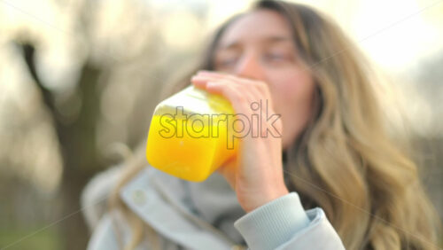 Video - Woman in a puffer jacket drinking orange juice in a park