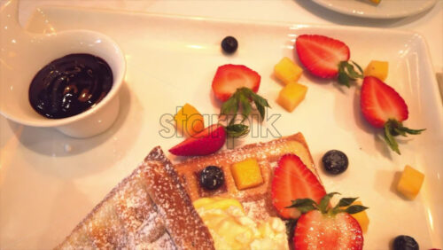 Video - Close up of waffles with fruit and jam on a white plate at a restaurant