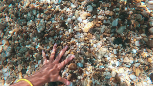 Video - Female hand taking rocks from the bottom of the Aegean sea visible through the clear water, refraction of light. Greece