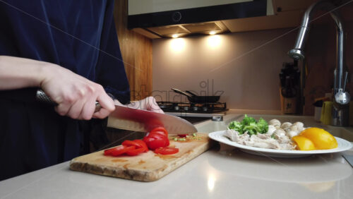 Video - Woman in a blue robe cutting up tomatoes on a wooden board in the kitchen