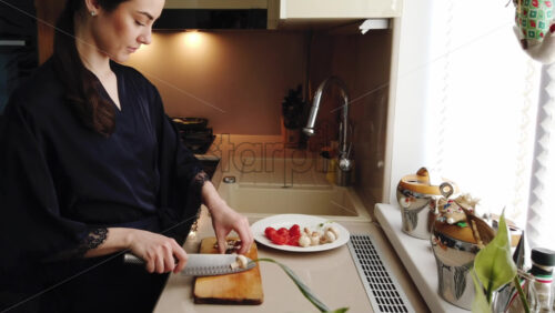 Video - Woman in a blue robe cutting up mushrooms on a wooden board in the kitchen