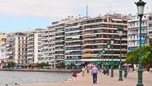 Video - THESSALONIKI, GREECE - SEPTEMBER 21, 2020: People hanging out together,sitting on the board of the sea, filling their needs, walking or cycling on the coast