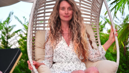 Video - A woman smiling and enjoying her vacation, resting in an armchair, swinging