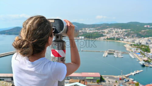Video - A woman in white t-shirt looking into and stationary binocular on the other shore of Kavala, Greece