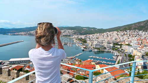 Video - A woman in white t-shirt looking into and stationary binocular on the other shore of Kavala, Greece