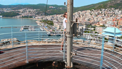 Video - A woman in white t-shirt on the view point is filming on smartphone, buildings, hills on the background, Kavala, Greece
