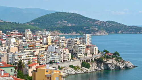 Video - Aerial view of Kavala. Rows of residential buildings, Aegean sea rocky coast, road with cars, hills on the background. Greece