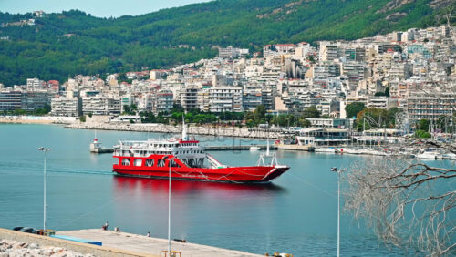 Video - KAVALA, GREECE - SEPTEMBER 23, 2020: Moving red ship near the Aegean sea coast, multiple buildings on the background
