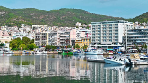 Video - KAVALA, GREECE - SEPTEMBER 23, 2020: Multiple buildings on the Aegean sea coast with port and moored yachts, green hill on the background
