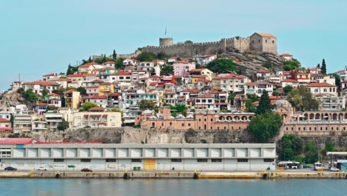 Video - KAVALA, GREECE - SEPTEMBER 23, 2020: View of the town from the water. Rows of residential buildings, ancient fortress on the hill, Aegean sea rocky coast