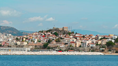 Video - KAVALA, GREECE - SEPTEMBER 23, 2020: View of the town from the water. Rows of residential buildings, ancient fortress on the hill, Aegean sea rocky coast