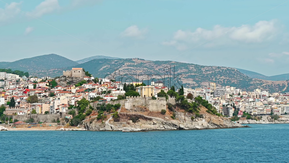 Video - View of Kavala from the water. Rows of residential buildings, ancient fortress and church on the hill, Aegean sea rocky coast. Greece