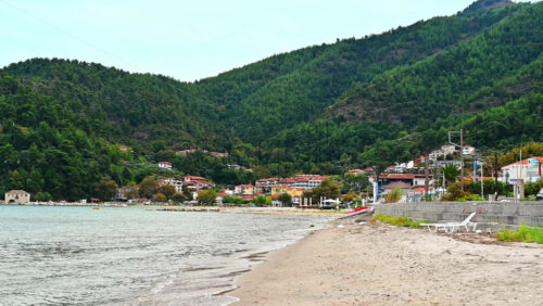 Video - THASOS, GREECE - SEPTEMBER 23, 2020: View of the Aegean sea coast, breakwater near the beach, town under the hill slope full of greenery