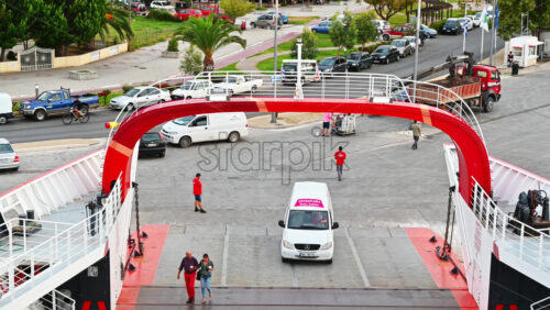 Video - THASOS, GREECE - SEPTEMBER 23, 2020: Moored ferryboat, opened gangplank in the port, road, walking people, town and parked cars on the background