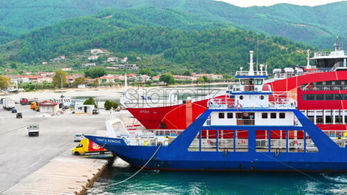 Video - THASOS, GREECE - SEPTEMBER 23, 2020: Moored ferryboats with blue and red exteriors, opened gangplanks in the port, cars are driving out of the ship