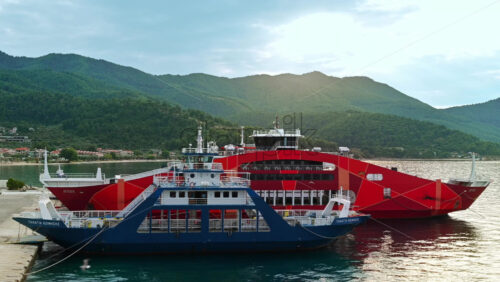Video - THASOS, GREECE - SEPTEMBER 23, 2020: Moored ferryboats with blue and red exteriors, opened gangplanks in the port, green hills on the background
