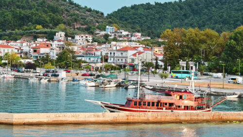 Video - THASOS, GREECE - SEPTEMBER 23, 2020: View of the Aegean sea coast, moored boats and an old yacht, town under the hill slope full of greenery