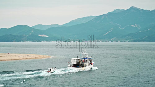 Video - THASOS, GREECE - SEPTEMBER 23, 2020: Moving tug carrying a boat with seething water. Hills on the background. Cloudy weather, sunset