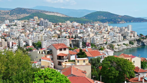 Video - Aerial view of Kavala. Rows of residential buildings, Aegean sea rocky coast, road with cars, viaduct, hills on the background. Greece