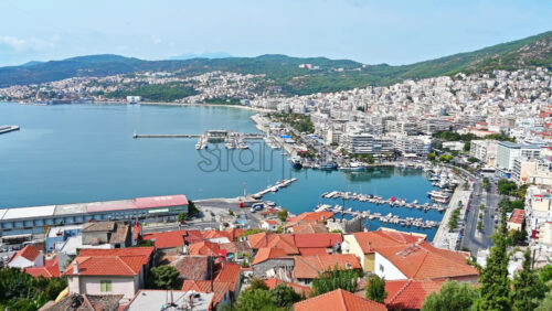 Video - Aerial view of Kavala. Rows of residential buildings, Aegean sea port with moored yachts, roads with people and cars, green hills on the background. Greece