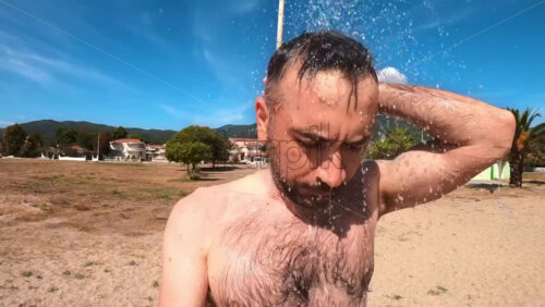 Video - Man taking shower on the beach of Asprovalta, town on the background, Greece