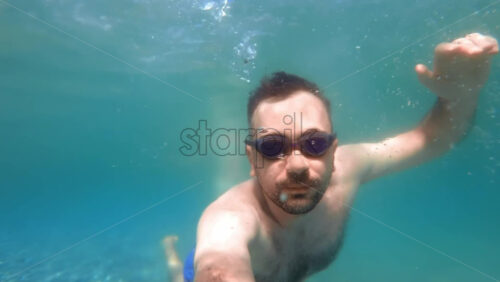 Video - Man in swimming goggles under the water and holding camera, Aegean sea. Slow motion, underwater shooting. Greece