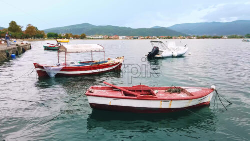 Video - STAVROS, GREECE - SEPTEMBER 26, 2020: Moored boats on the shore of the Aegean sea, town and hills on the background, cloudy sky