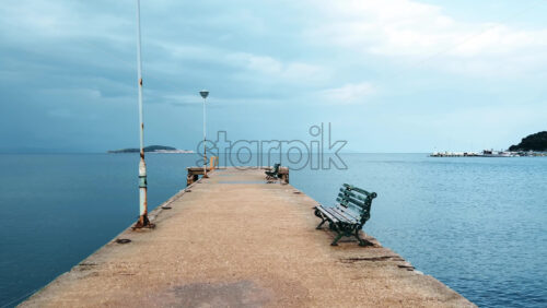Video - Pier with lamp posts, benches near the Aegean sea coast in Stavros, hills on the background, Greece