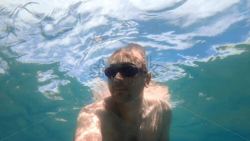 Video - Man in swimming goggles under the water and holding camera, Aegean sea. Slow motion, underwater shooting. Greece