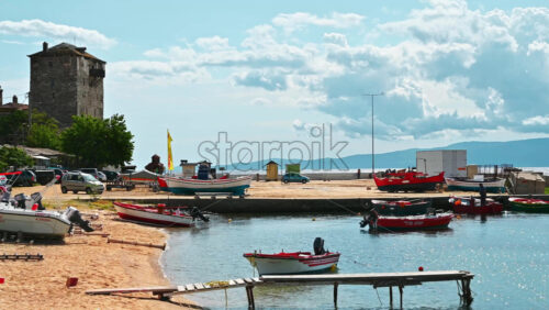 Video - OURANOUPOLIS, GREECE - OCTOBER 2, 2020: Sea port, moored boats on Aegean sea, few parked cars, two small wooden piers, hills on the background and Tower of Prosphorion