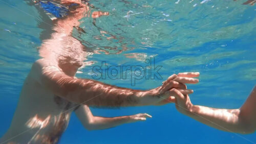 Video - Man and woman holding hands under the water, Aegean sea. Slow motion, underwater shooting. Greece
