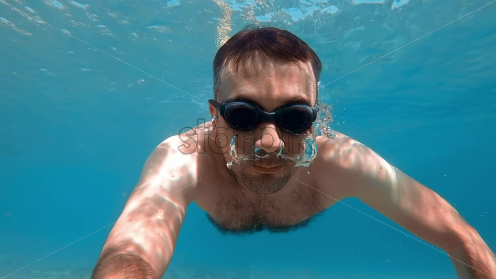 Video - Man in swimming goggles under the water and holding camera, Aegean sea. Slow motion, underwater shooting. Greece