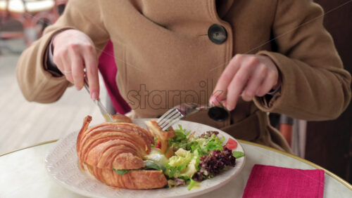 Video - Woman in brown coat eating a poached egg croissant with salad at a restaurant