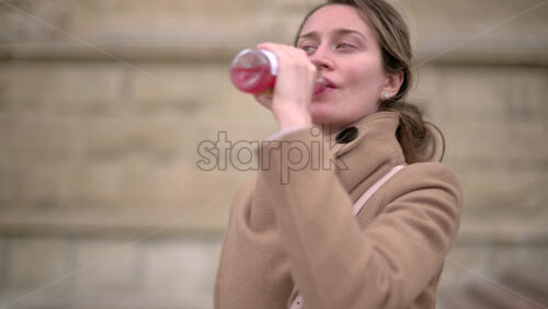 Video - Woman in brown coat drinking a pink beverage outside