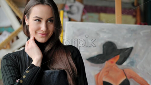 Video - Woman painter wearing black clothes painting woman model face with hat drawing with red brush at a workshop