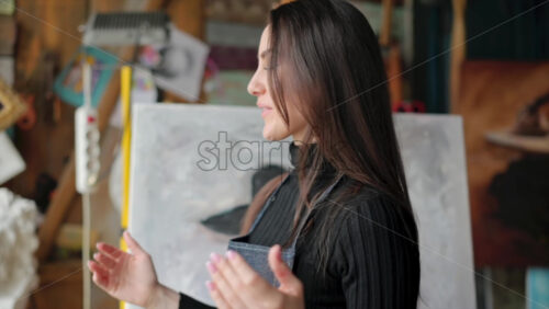 Video - Woman painter wearing black clothes painting woman model face with hat drawing with red brush at a workshop
