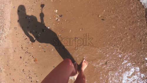 Video - Caucasian woman walking along the coast in slow motion holding camera and filming legs, Asprovalta, Greece